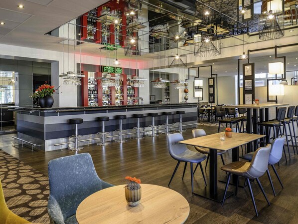 Un área de bar moderna con techo alto, diversas opciones de asientos y una escalera visible.