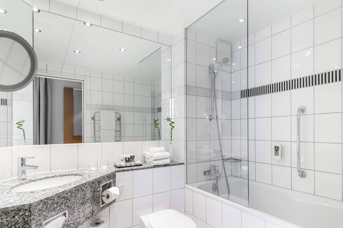 A modern bathroom with a granite countertop, a toilet, a glass-enclosed shower, and a large mirror.