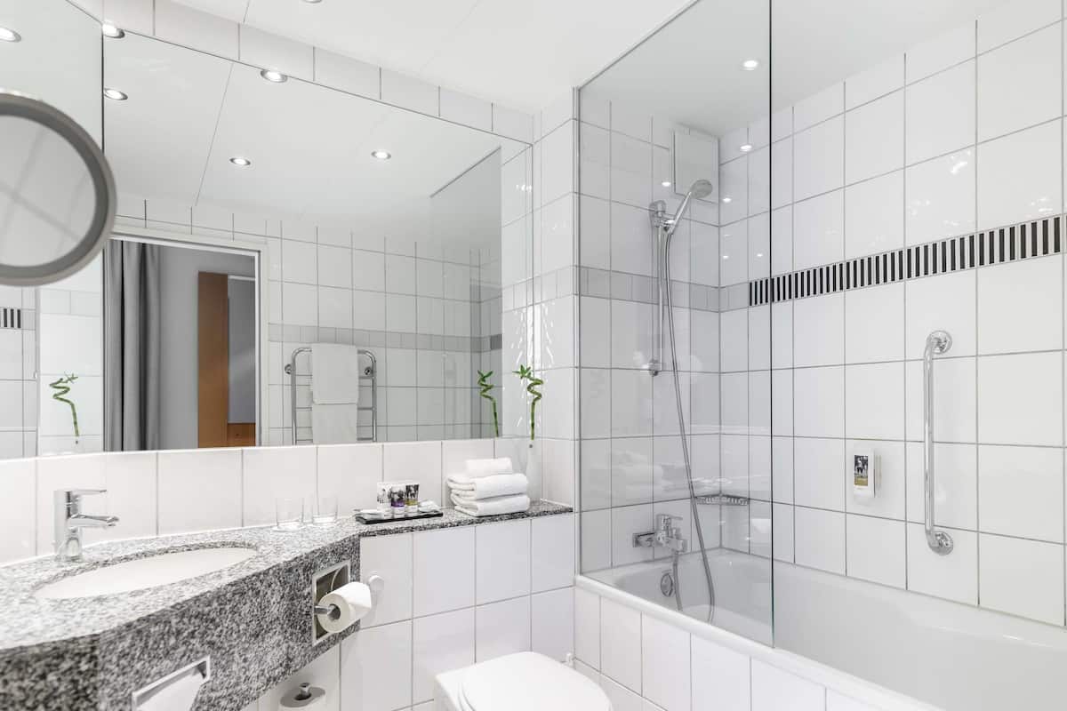 Un baño moderno con encimera de granito, inodoro, ducha con mampara de vidrio y un espejo grande.