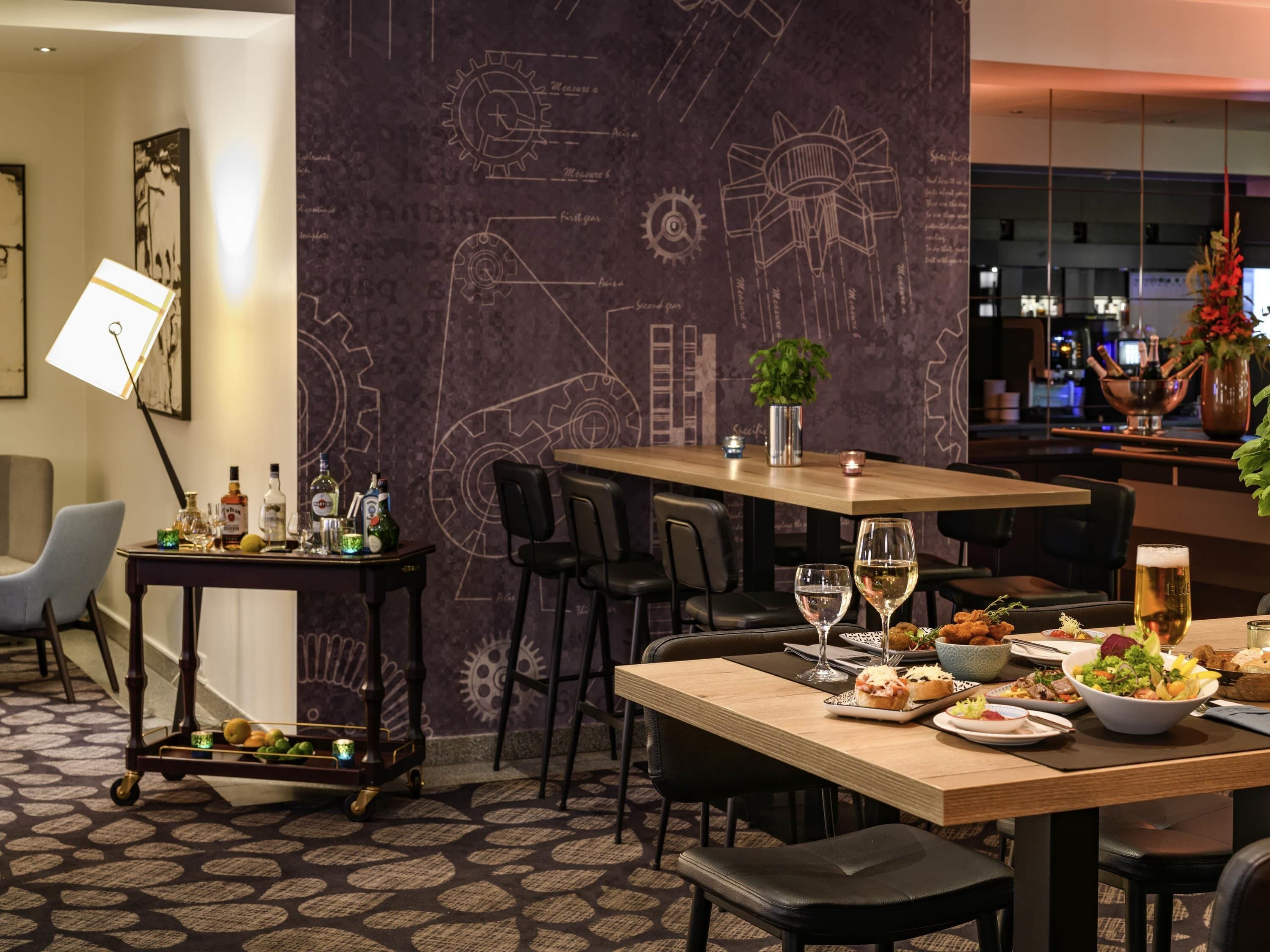 Ein Essbereich mit Tisch für zwei Personen, eine Bar und eine Wand mit technischen Zeichnungen.