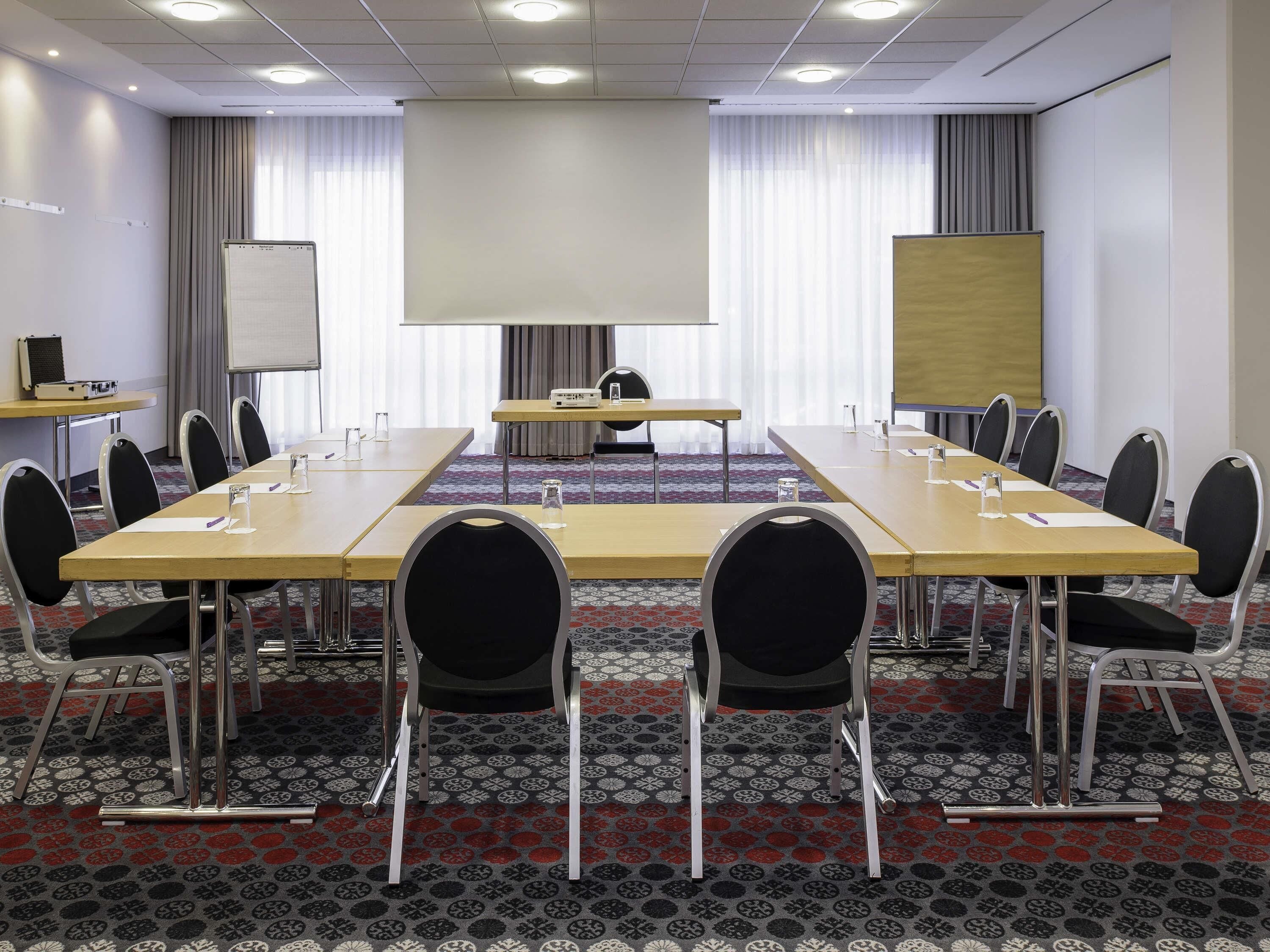 A conference room with a long table, chairs, a projector screen, and a whiteboard.
