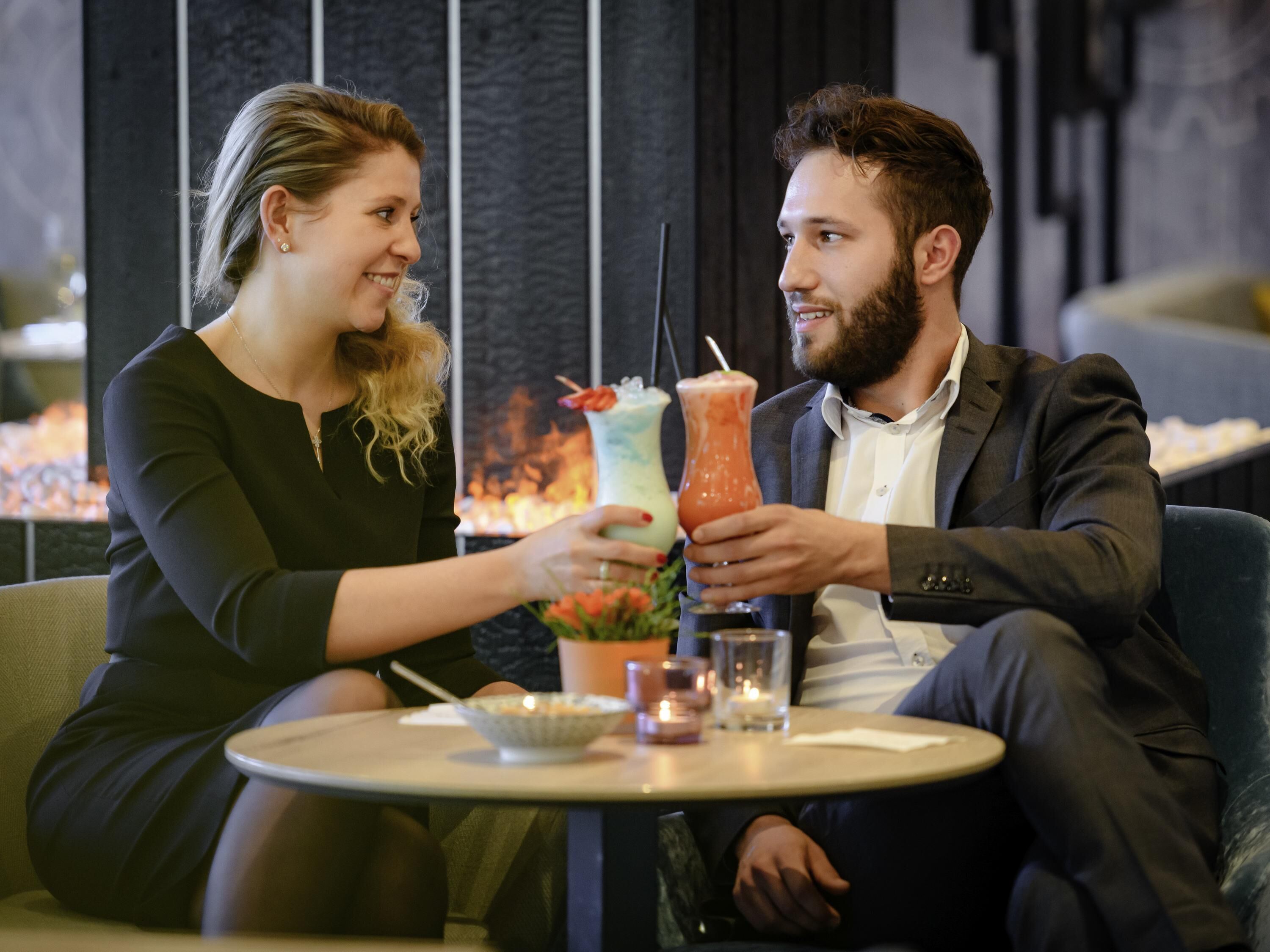 Dos personas sentadas en una mesa redonda con bebidas, en un interior moderno con líneas verticales en la pared.