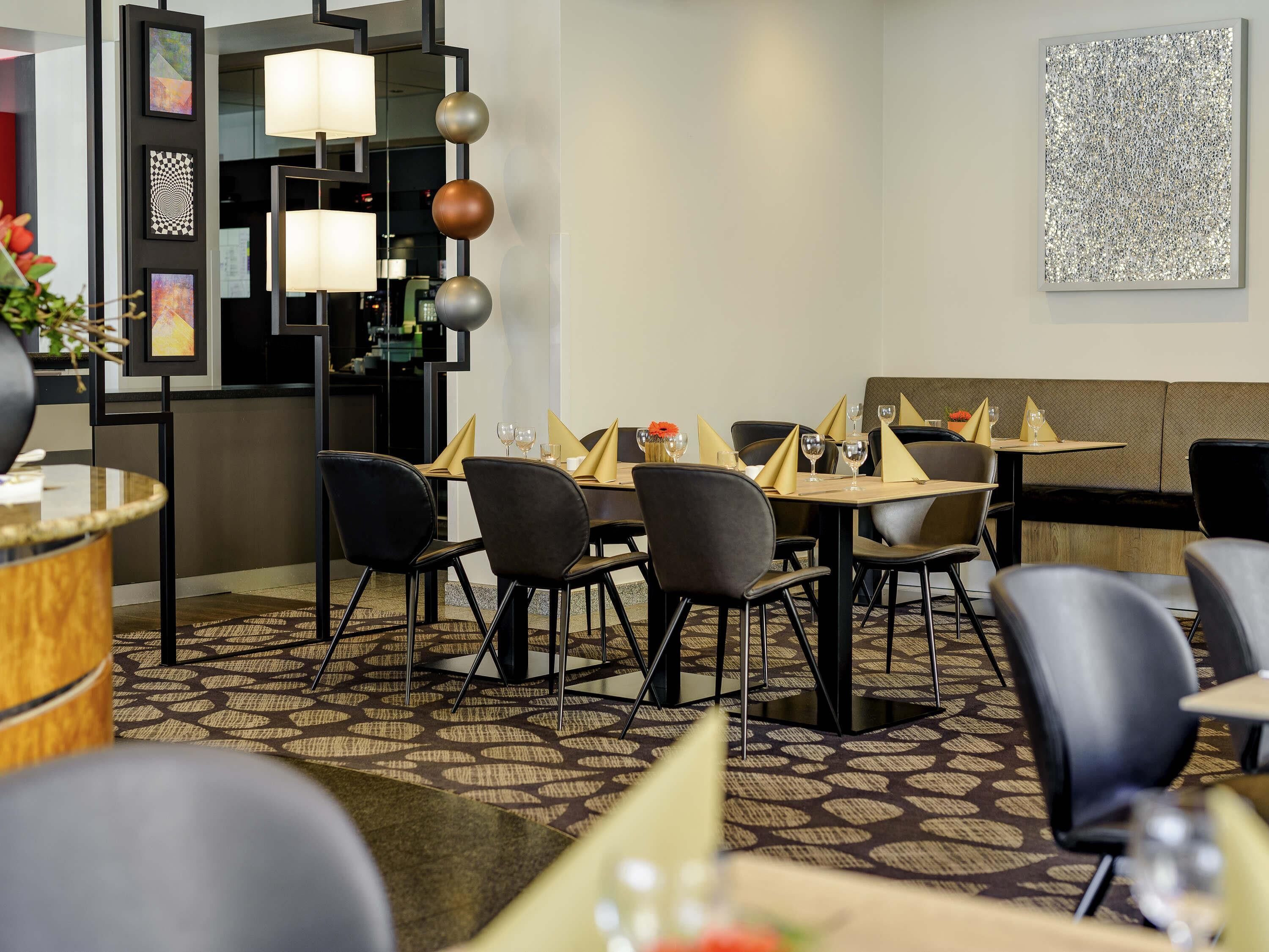 Un restaurant amb un interior modern, que destaca un mosaic de moqueta, cadires negres i una taula de menjador preparada amb vasos i sergetes.