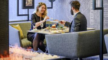 Un coin repas avec une table dressée pour deux personnes, un canapé et un mur décoratif orné de motifs abstraits.