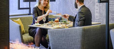 Un comedor con mesa lista para dos personas, un sofá y una pared decorativa con diseños abstractos.