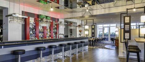 A modern bar area with multiple stools, a bar counter, and a variety of bottles and glasses.