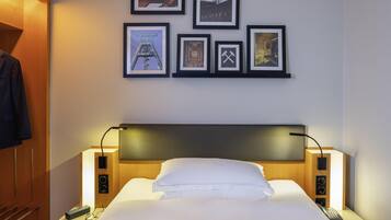 A hotel room with a bed, bedside lamps, a nightstand, a remote control, and framed pictures on the wall.