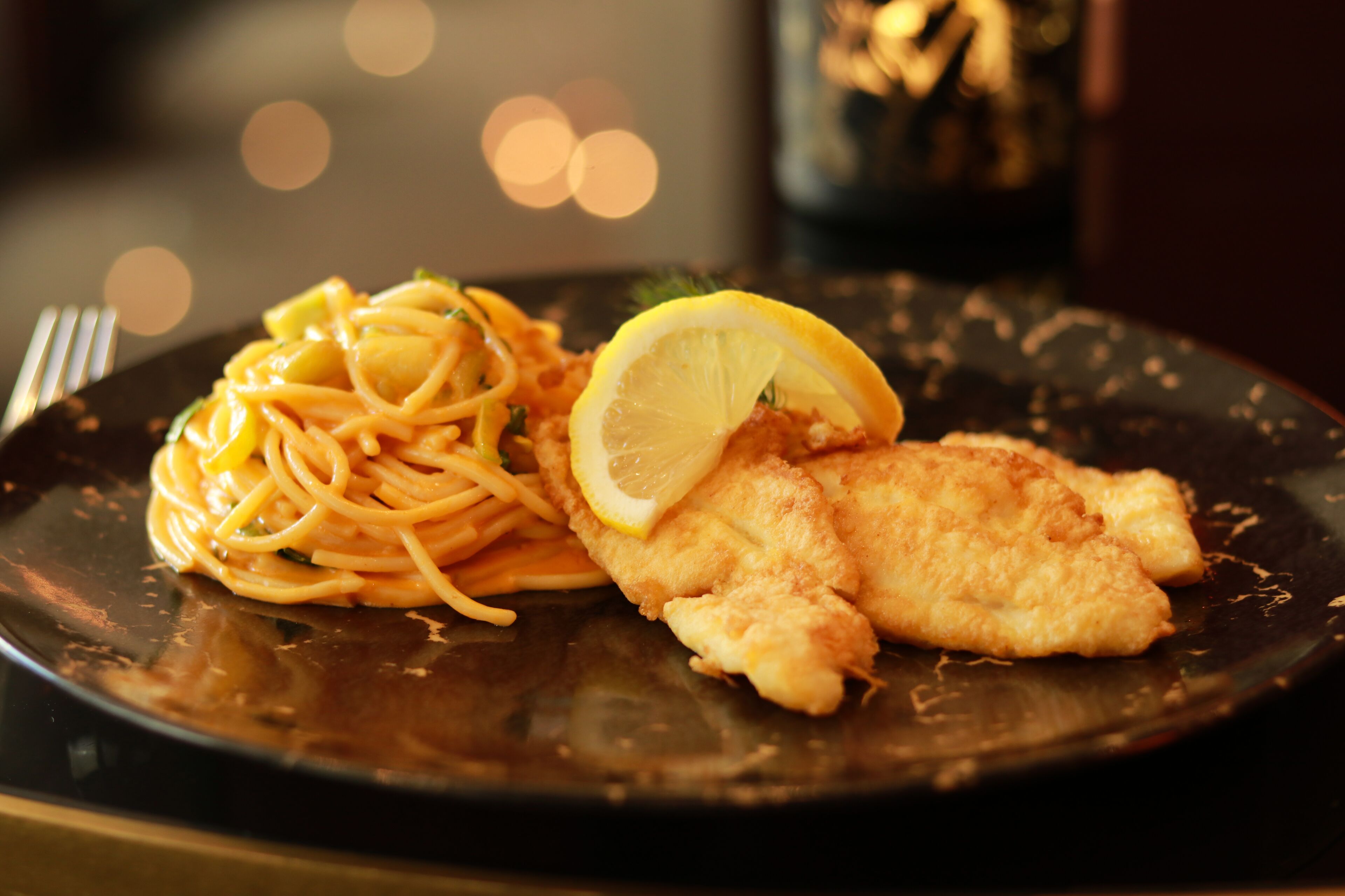 A plate of food with spaghetti and a breaded cutlet, garnished with a lemon slice.