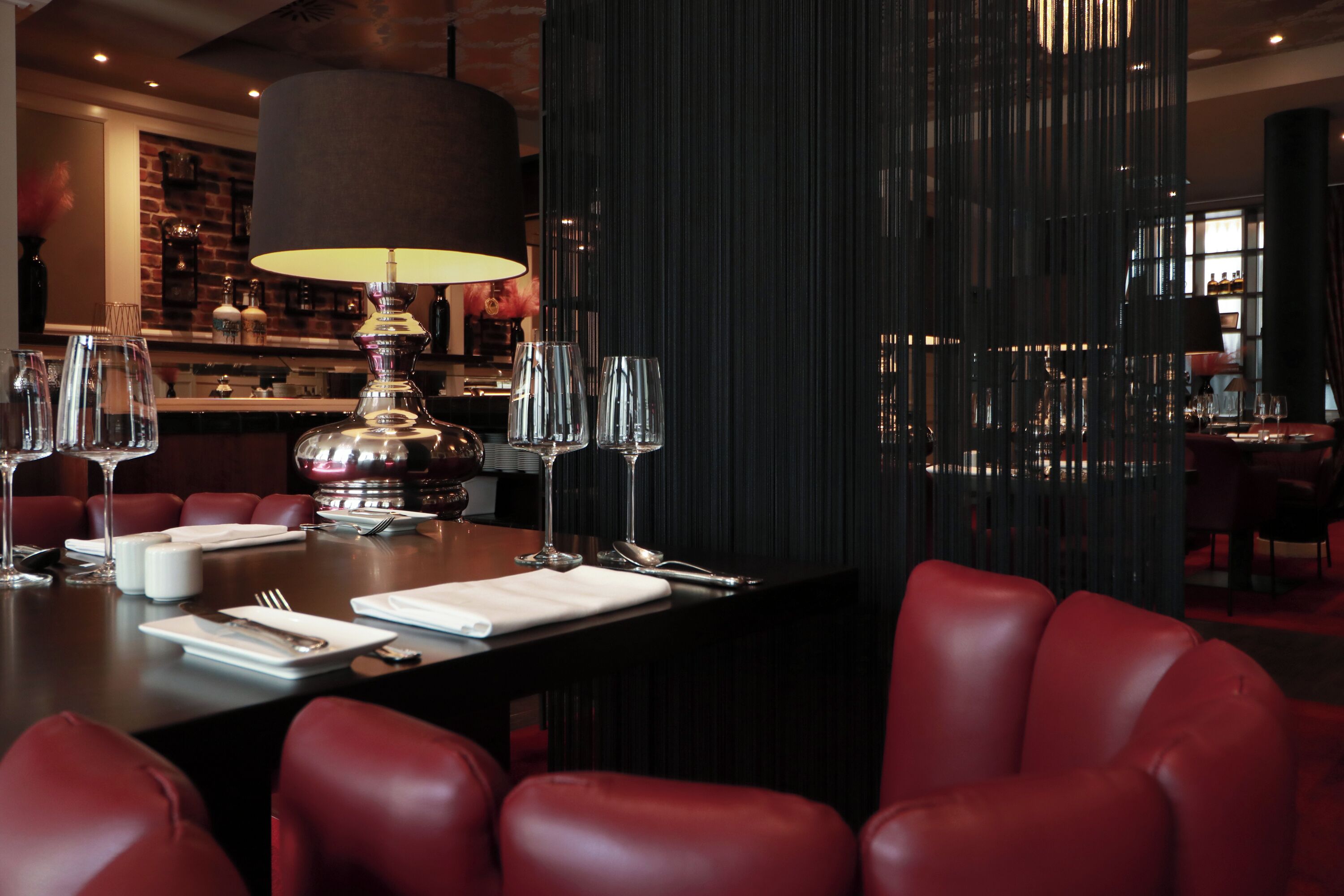 Un restaurant à l’intérieur sombre, avec des fauteuils en cuir rouge, une table dressée avec des verres à vin, des assiettes et des couverts.