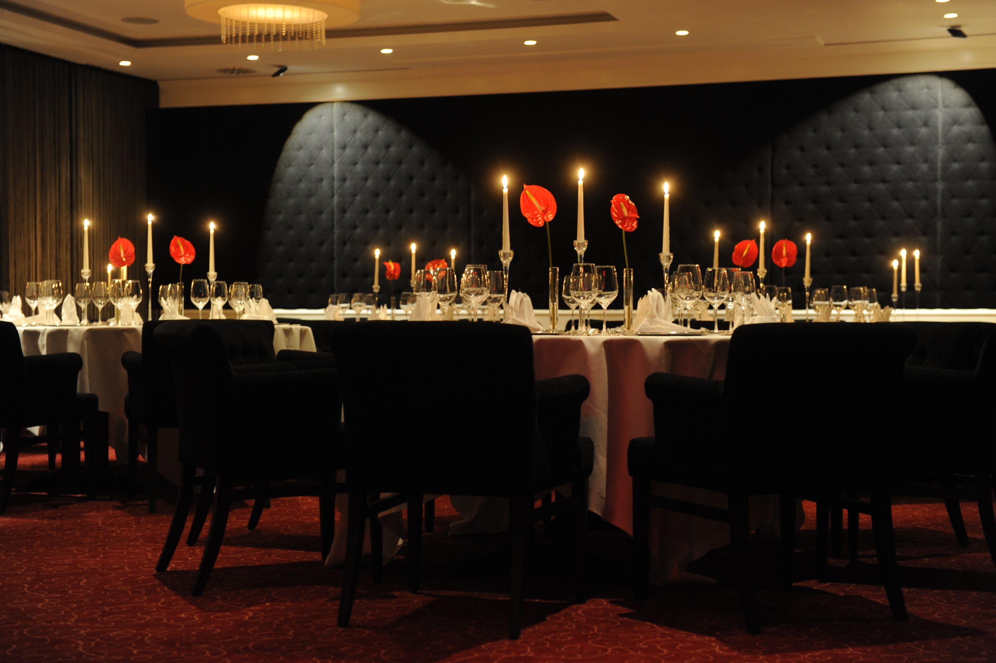A formal dining room with tables set for multiple guests, featuring candles and glassware.