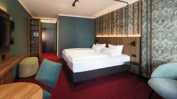 A hotel room with a large bed, a desk, a chair, a small table, a wardrobe, and a TV.
