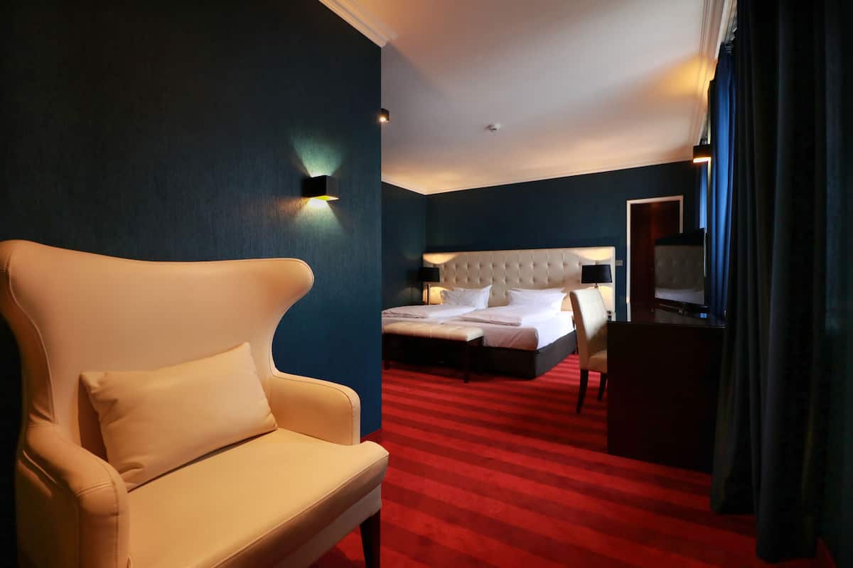 A hotel room with a large bed, a chair, a desk, and a red carpet.