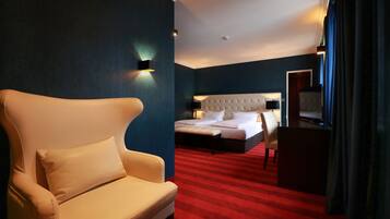 A hotel room with a large bed, a chair, a desk, and a red carpet.