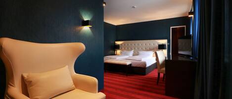 A hotel room with a large bed, a chair, a desk, and a red carpet.