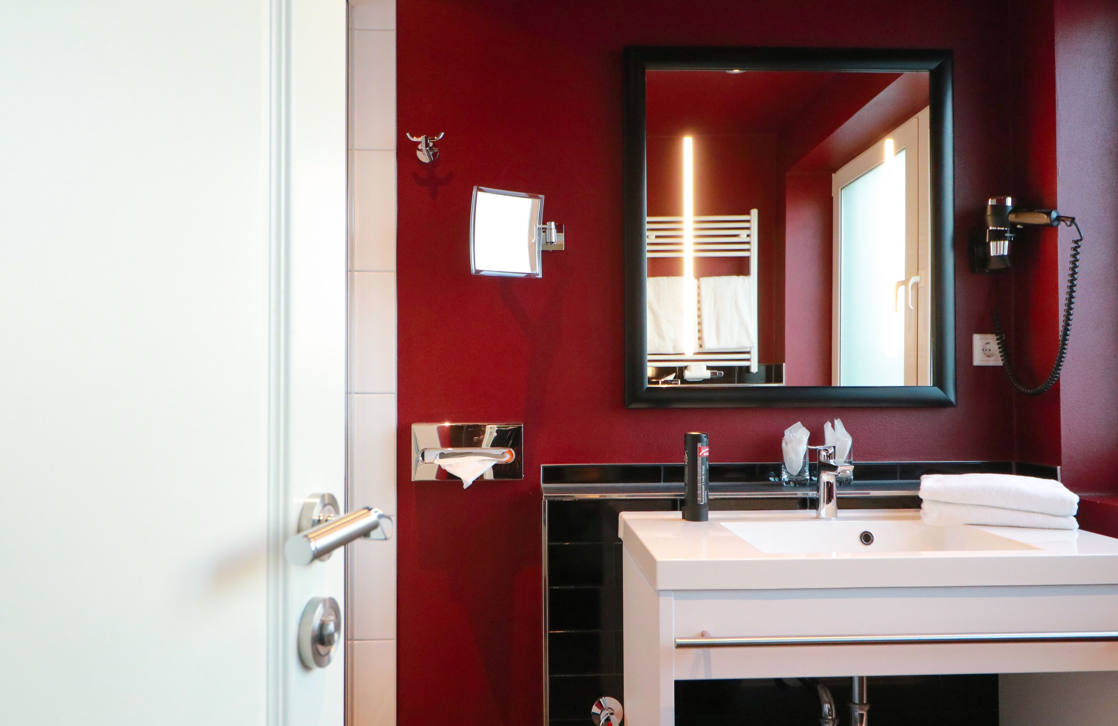 A modern bathroom with a red wall, a white sink, a mirror, and a telephone.