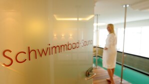 A spa area with a sign reading "Schwimmbad-Sauna" and a person in a bathrobe standing by a wooden deck. - Hotel Haverkamp (Bremerhaven)