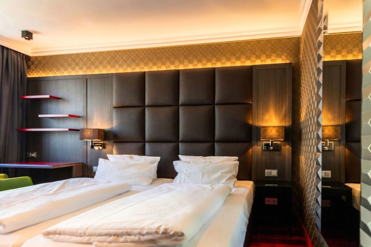 Una habitación de hotel con una cama grande, dos mesitas de noche, un escritorio y una silla.