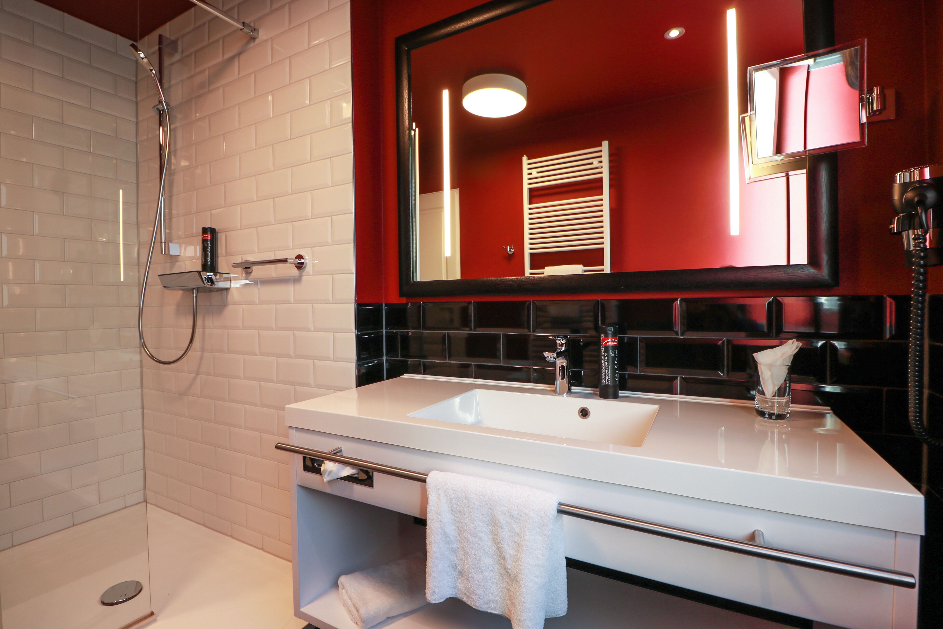 A modern bathroom with a white sink, a glass shower enclosure, and a red accent wall.