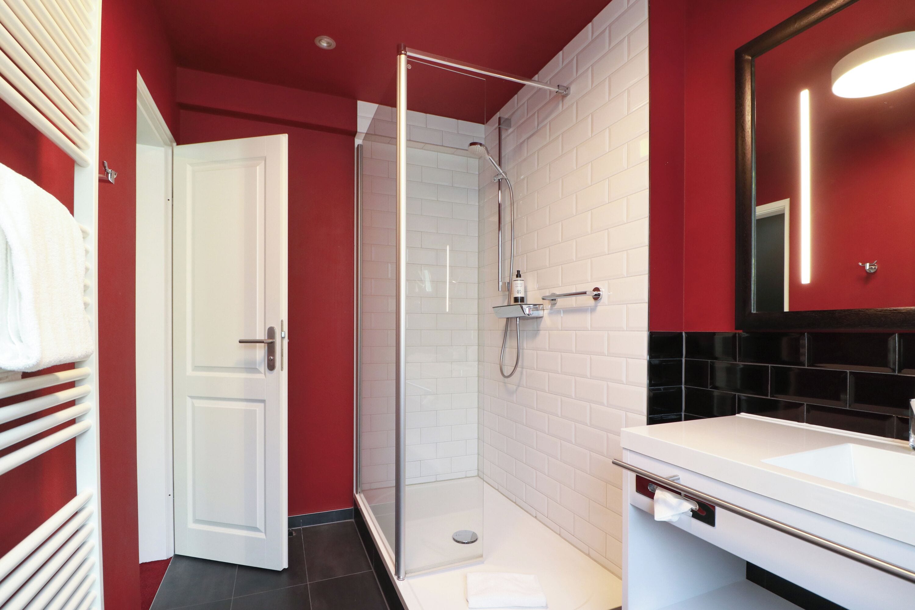 Un baño con cabina de ducha de vidrio, un lavabo blanco y una pared roja.