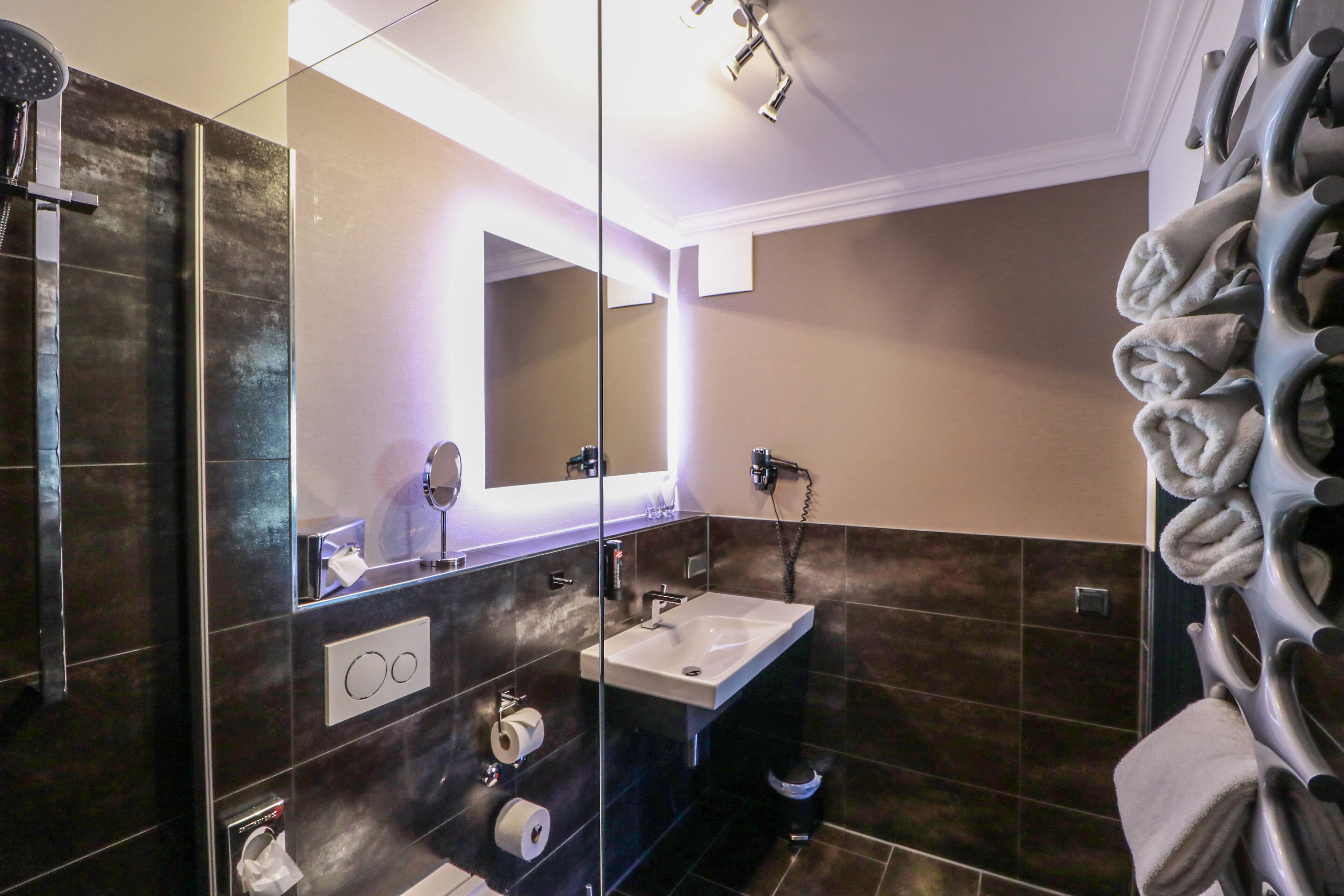 Un bagno moderno con pareti divisorie in vetro, un lavandino, uno specchio e un porta asciugamani.