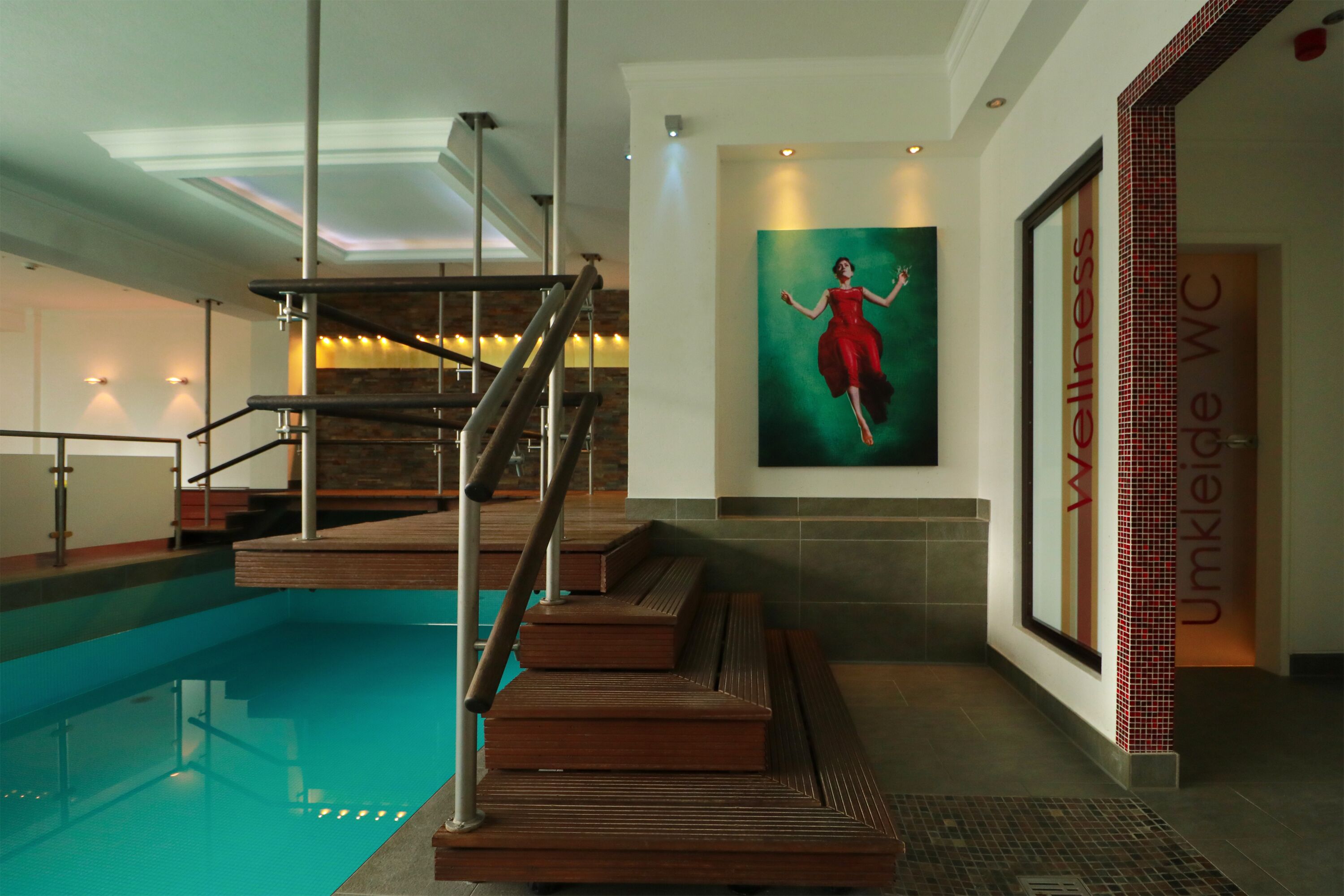 A modern indoor pool area with a wooden staircase leading to a platform over the pool.