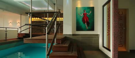 A modern indoor pool area with a wooden staircase leading to a platform over the pool.