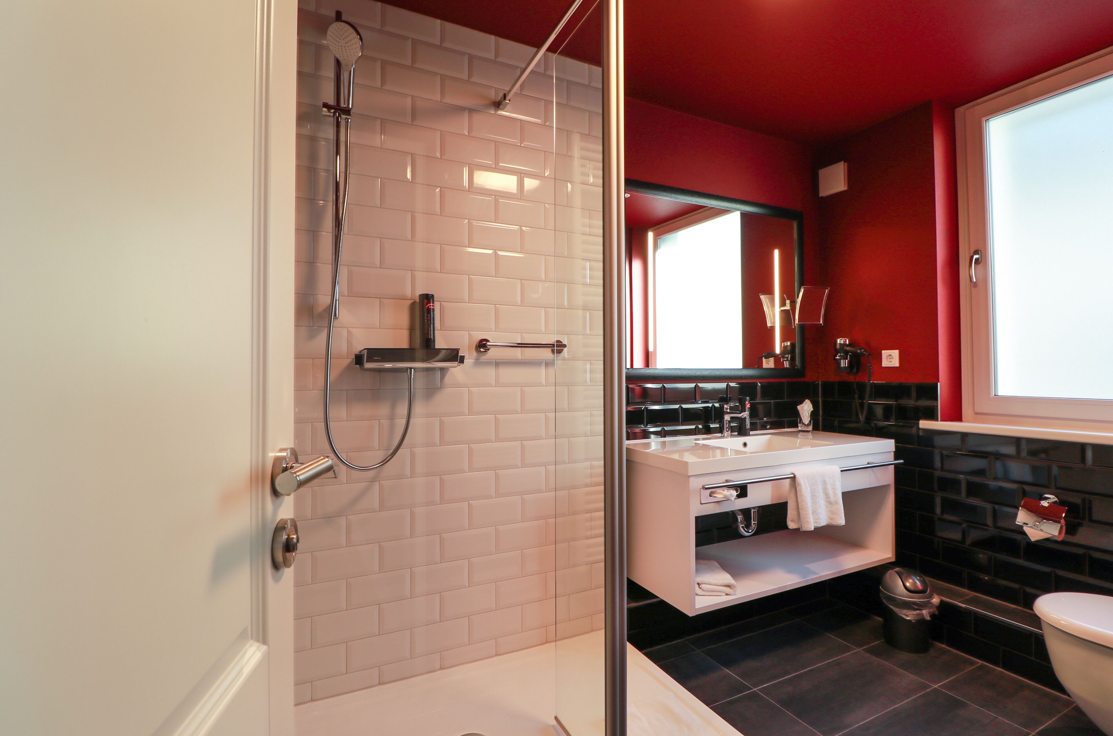 A modern bathroom with a glass-enclosed shower, a white sink, and a black tiled floor.