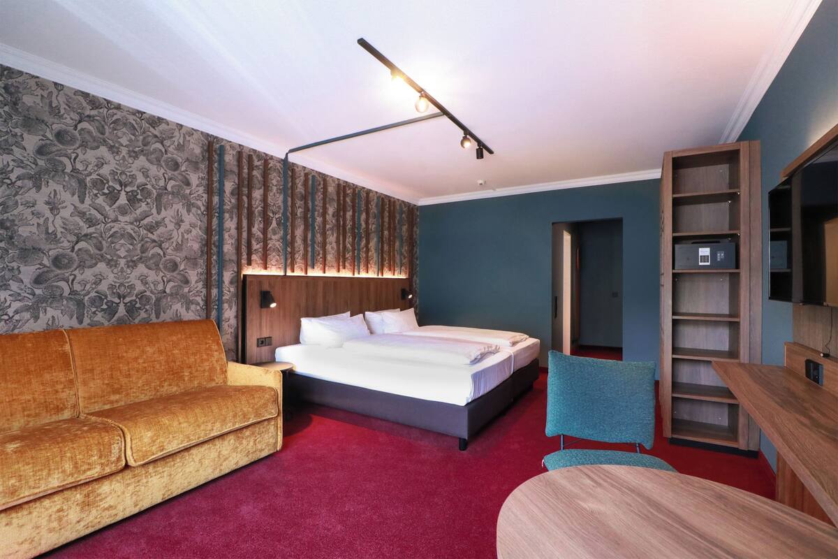 A bedroom with a bed, a sofa, a chair, a desk, and a bookshelf.