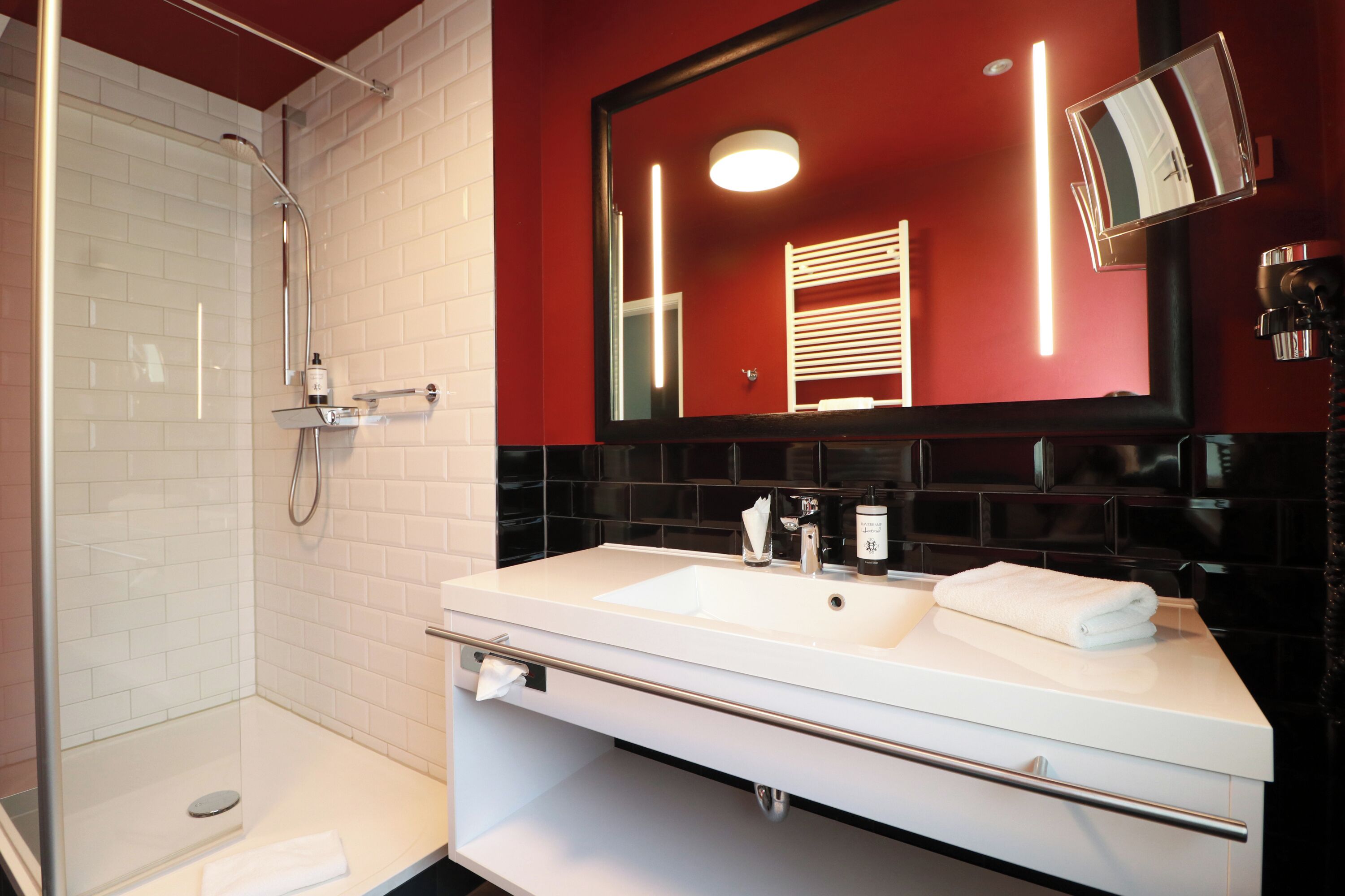 Un baño moderno con ducha de vidrio, un lavamanos blanco con espejo y una pared de acento roja.