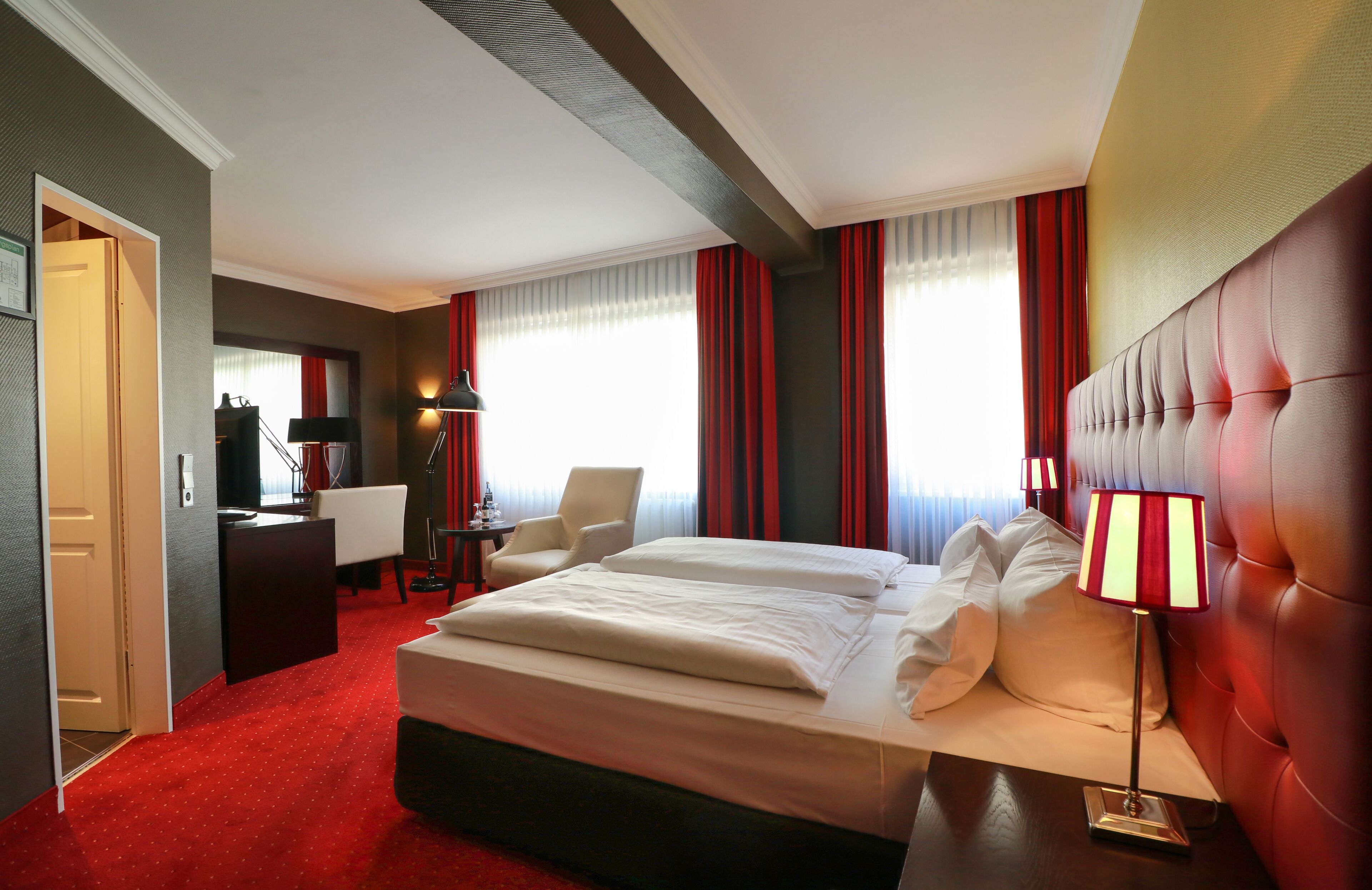 A hotel room with a large bed, a desk, a chair, and a lamp.