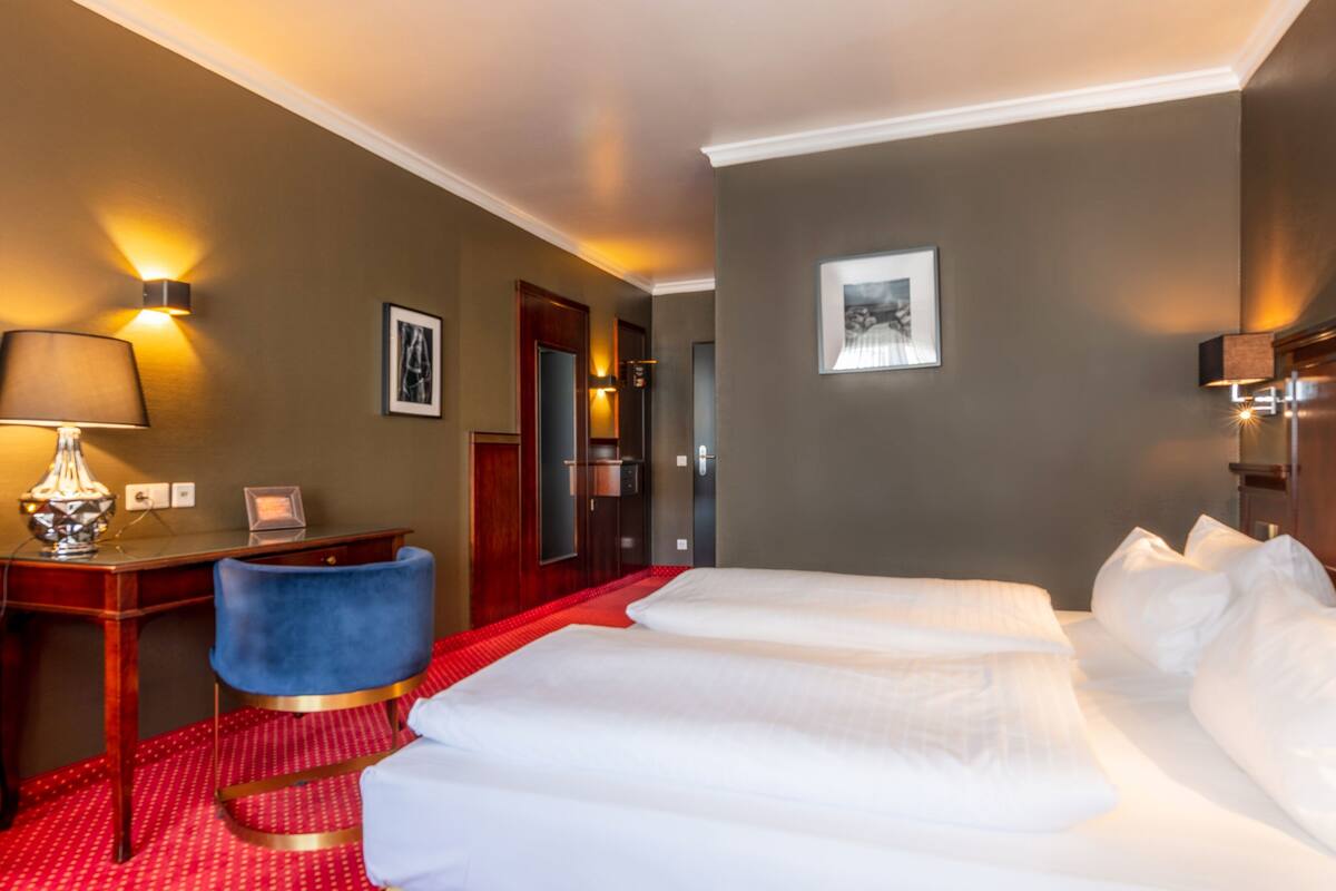 A hotel room with a bed, a desk, a chair, and a door.