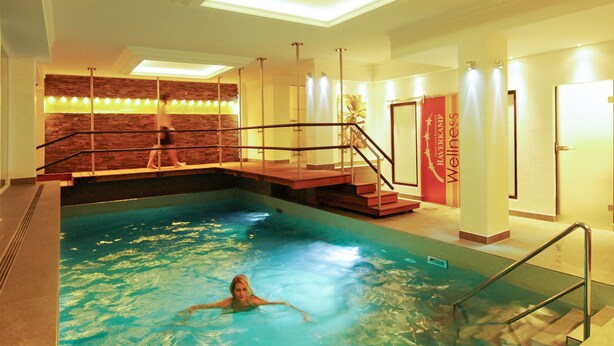 An indoor swimming pool with a person swimming, a brick wall, and a staircase leading to a higher level. - Hotel Haverkamp (Bremerhaven)