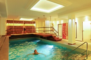 Una piscina interior con una persona nadando, un muro de ladrillo y una escalera que sube a un nivel superior.