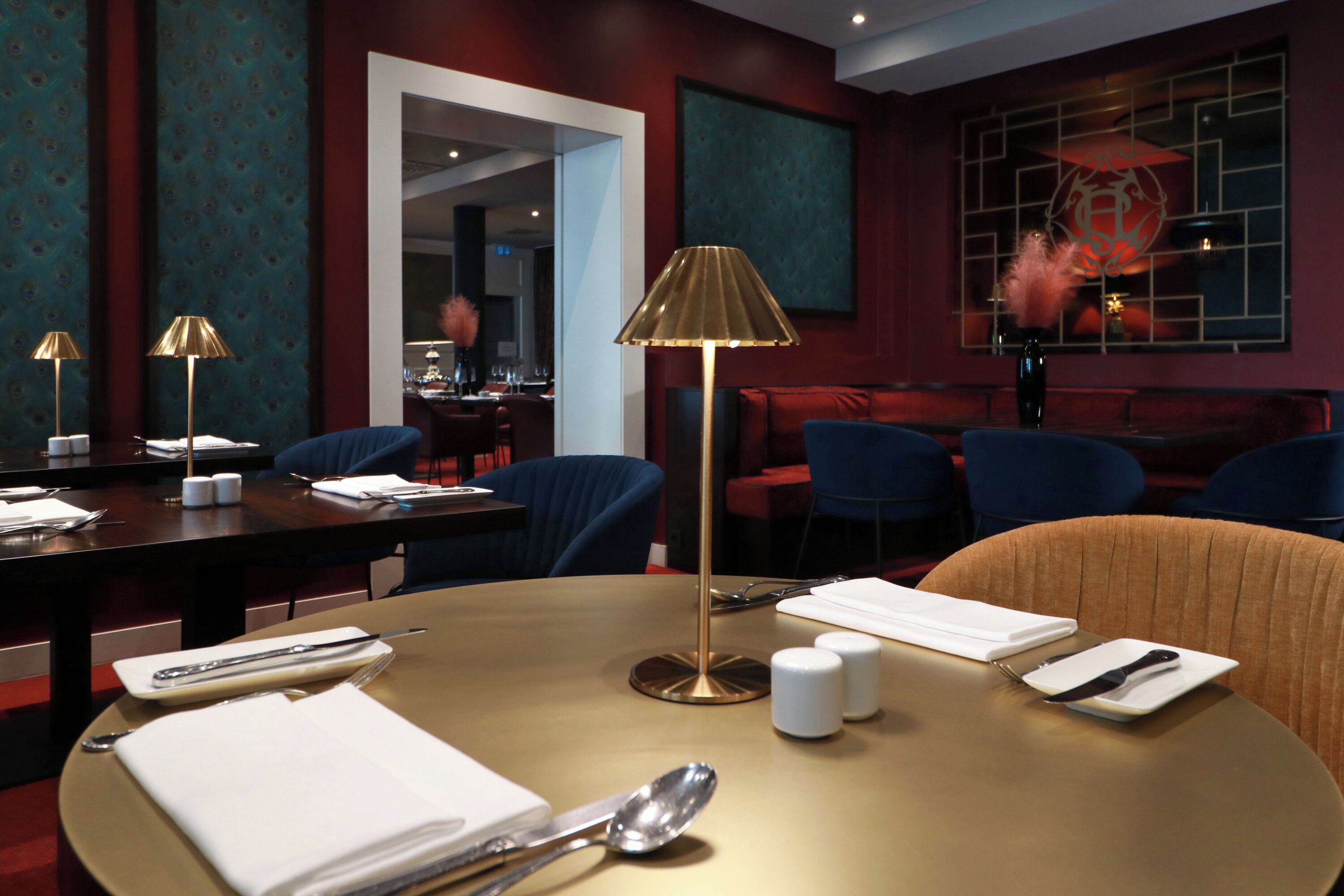 A restaurant with a round table set for dining, a gold lamp, and blue chairs.