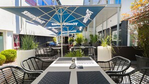 An outdoor seating area with tables and chairs, umbrellas, and potted plants. - Hotel Haverkamp (Bremerhaven)