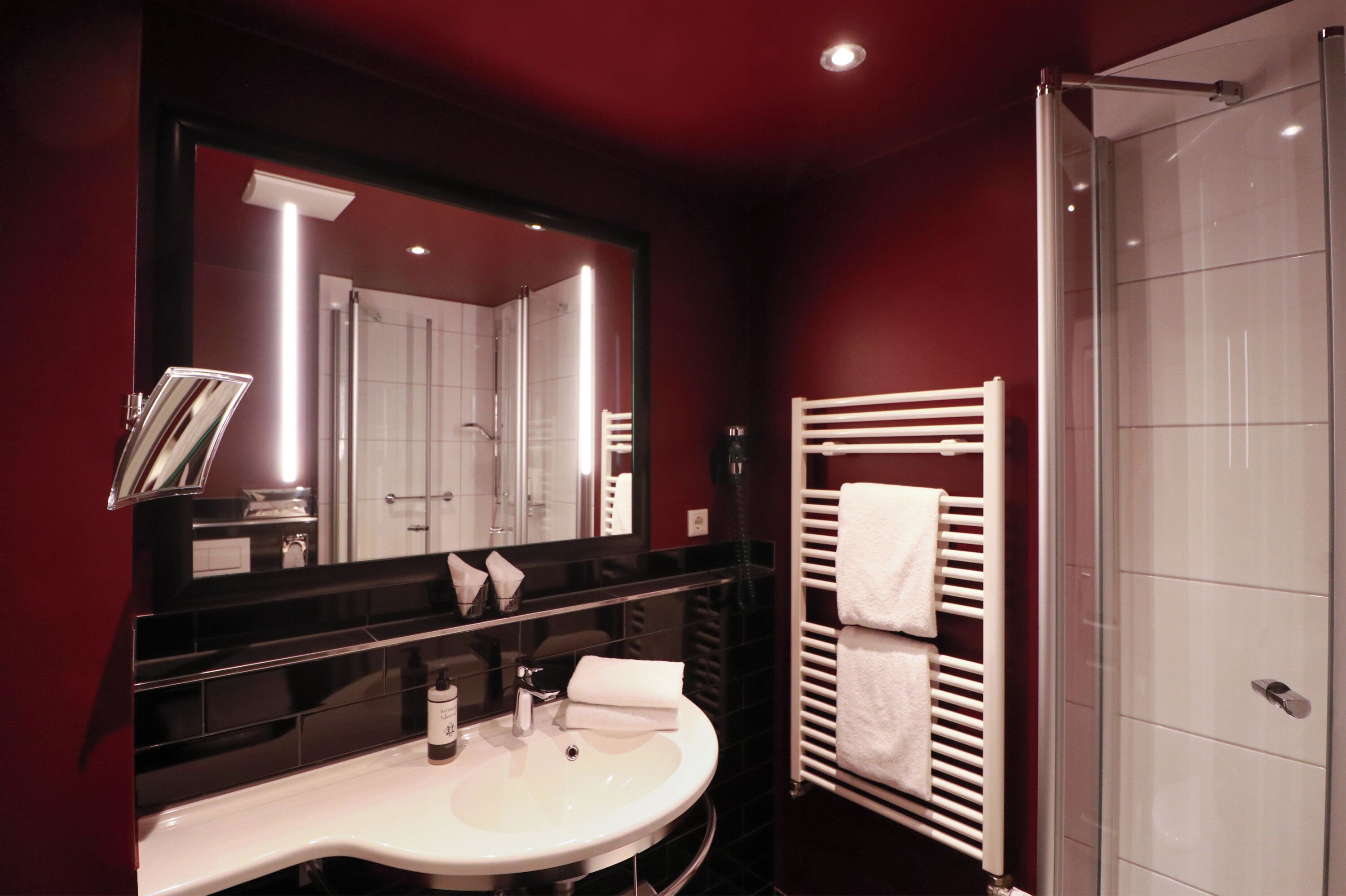 A modern bathroom with a large mirror, a white sink, a towel rack, and a glass shower enclosure.