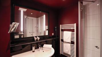A modern bathroom with a large mirror, a white sink, a towel rack, and a glass shower enclosure.