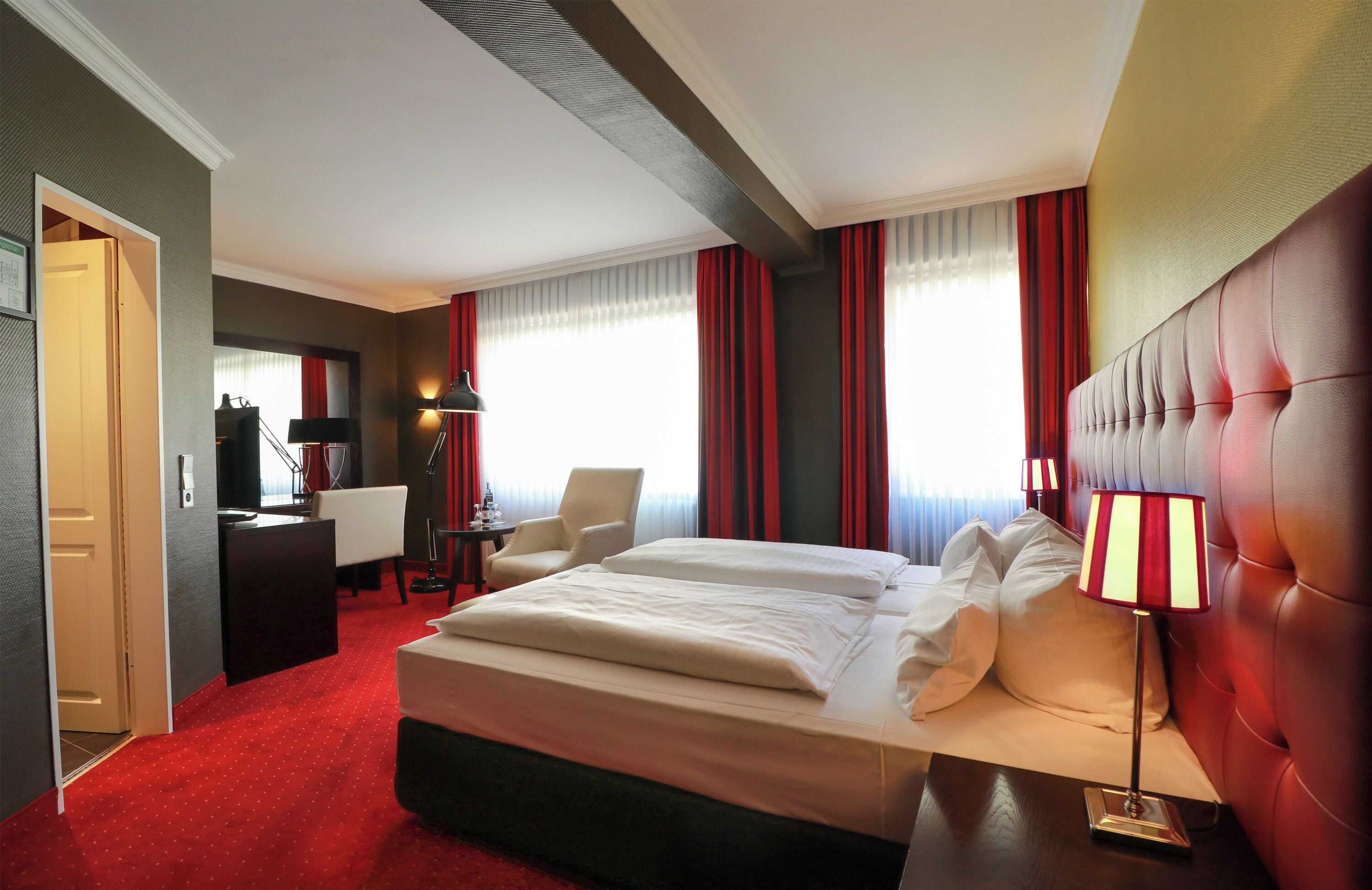 A hotel room with a large bed, a desk, a chair, and a lamp.