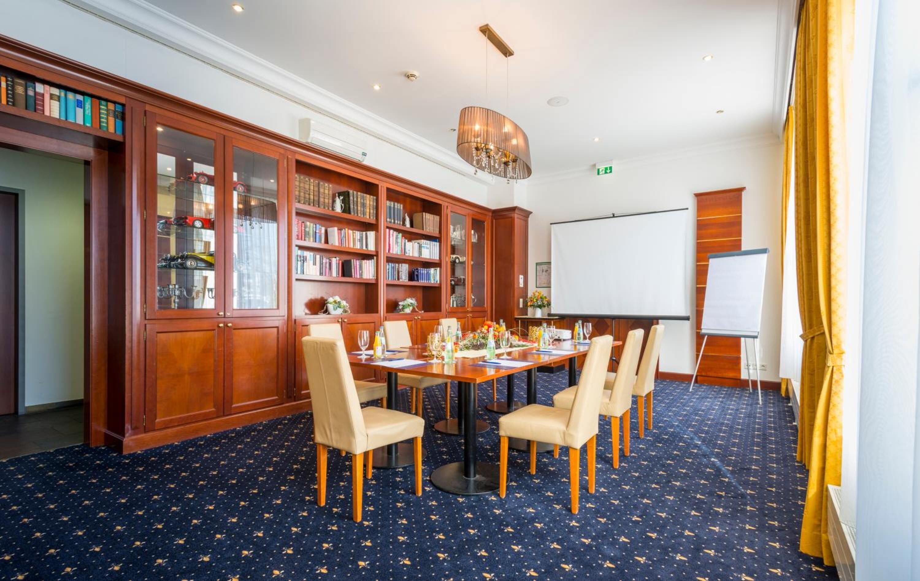 Un salón de conferencias con una gran mesa, sillas, una pantalla de proyector y estanterías.