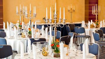 Ein Festsaal mit runden Tischen, gedeckt für eine formelle Veranstaltung, mit weißen Tischdecken, silbernen Kerzenständern und blauen Stühlen.
