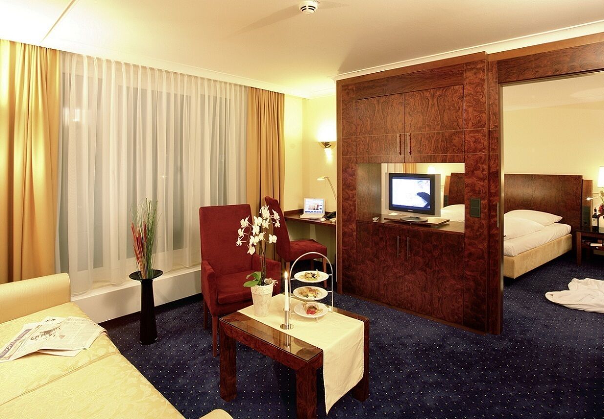 A hotel room with a bed, a TV, a desk with a vase of flowers, and a chair.