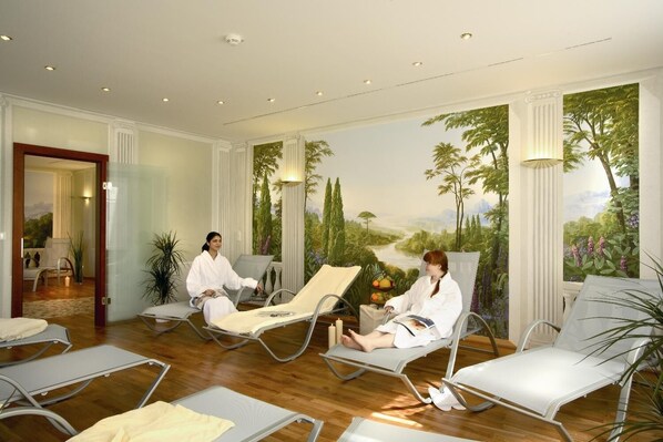 A spa room with two reclining chairs, a mural of a landscape, and a door leading to another room. - Hotel Glöcklhofer (Burghausen)