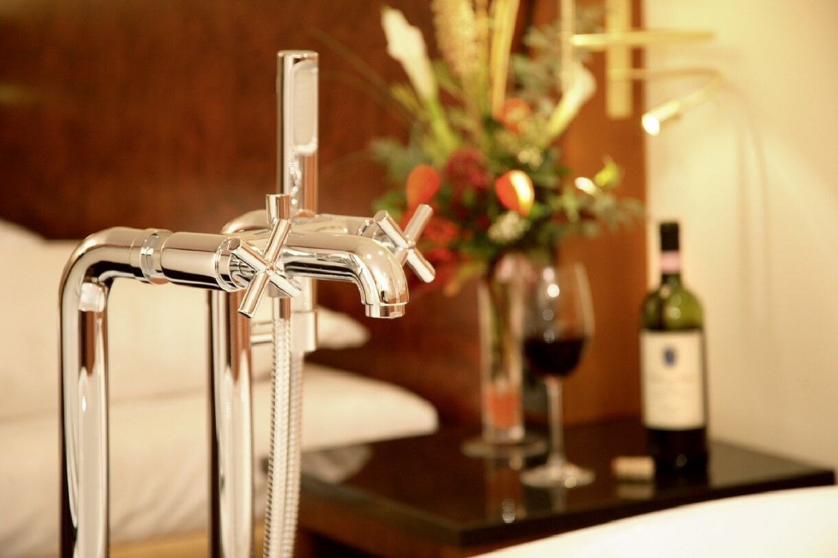 Un baño moderno con grifo cromado, cabina de ducha de vidrio y mesita de noche con botella de vino y copa.