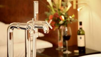 A modern bathroom with a chrome faucet, a glass shower enclosure, and a bedside table with a wine bottle and glass.