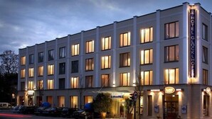 Un hotel de varios pisos con un diseño arquitectónico clásico, que presenta una entrada destacada con un letrero y una fachada bien iluminada.