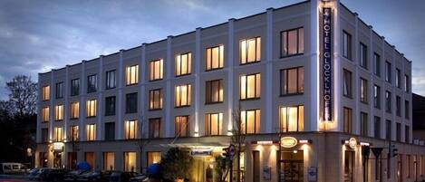 A multi-story hotel with a classic architectural design, featuring a prominent entrance with a signboard and a well-lit facade.
