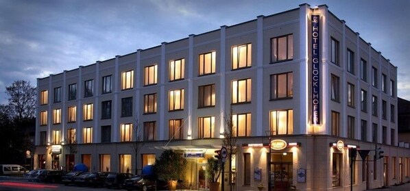 Un hotel de varios pisos con un diseño arquitectónico clásico, que presenta una entrada destacada con un letrero y una fachada bien iluminada.