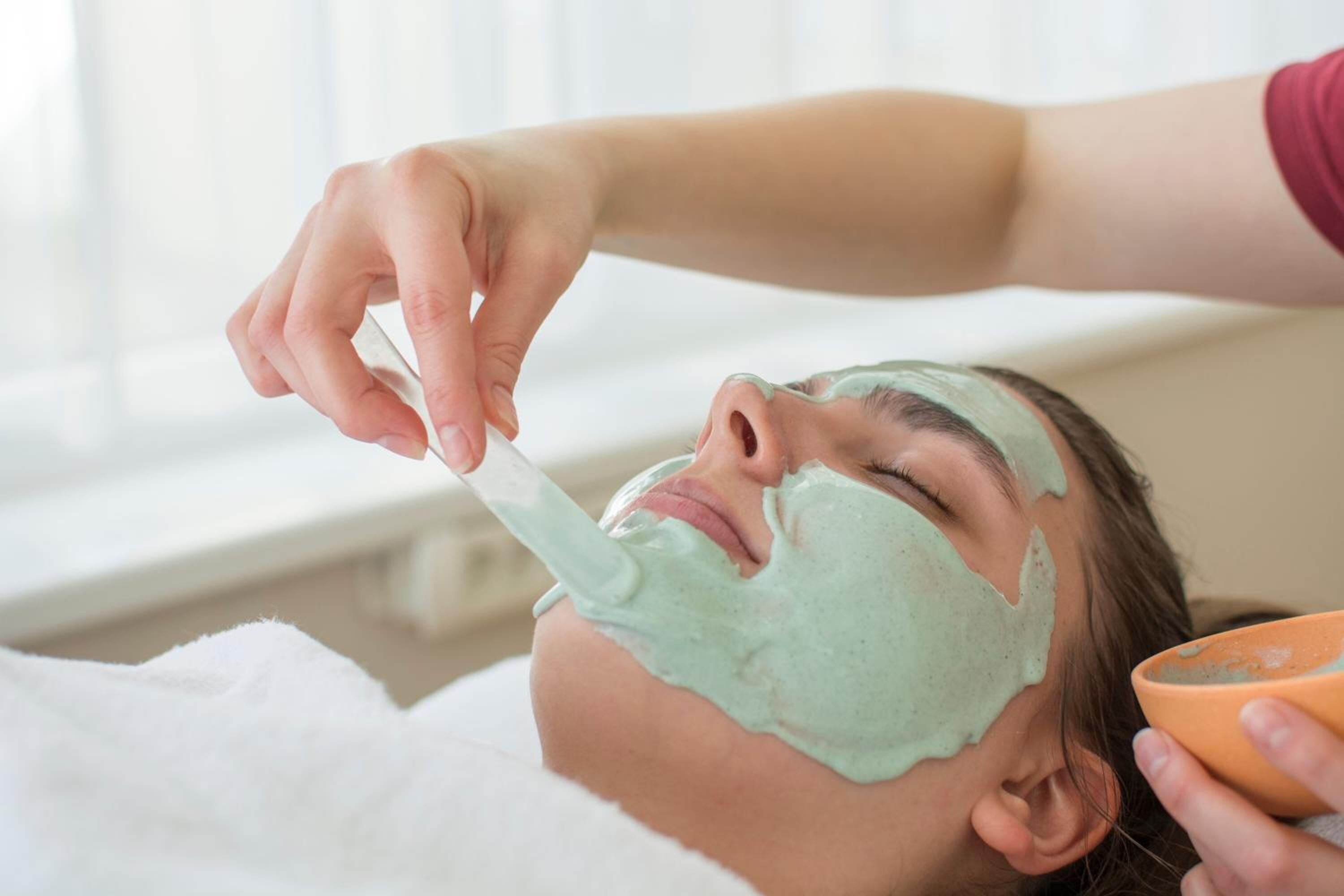 Una persona recibiendo un tratamiento facial con una mascarilla verde.