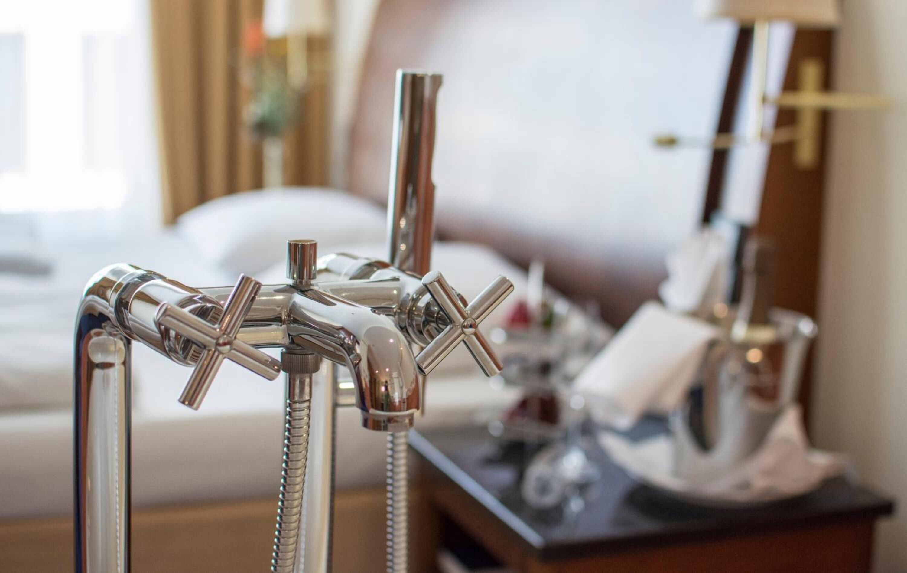 A hotel bathroom with multiple shower heads and a bedside table with a lamp and a phone.
