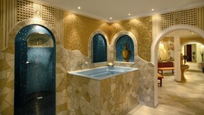 Un baño lujoso con una bañera grande, paredes de mosaico y arcos decorativos.